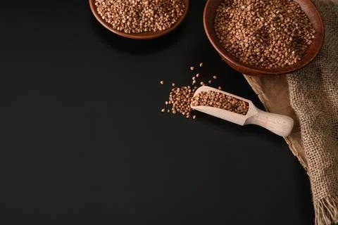 Buckwheat seeds in a wooden spoon and in bulk on a black background, selective Stock Photos
