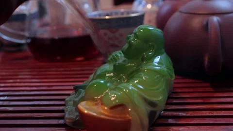 Buddha figurine on tray while brewing tea, which gradually changes color due to Stock Footage 276458467