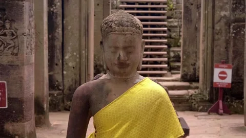 Buddha statue made of stone wearing golden robes is standing peacefully in Bayon Stock Footage 318704589