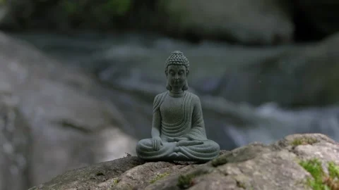 A Buddha statue sits on a rock in a mountain stream meditating Stock Footage 241150871