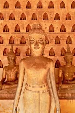Buddha statues in front of a wall filled with many miniature buddha figurin.. Stock Photos