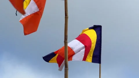Buddhist flag moves on a high flagpole with a gray clouded sky behind, showing Stock Footage 329276137