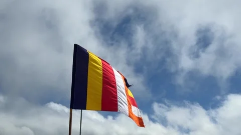 Buddhist flag waves on a tall pole against a cloudy sky, its bright stripes Stock Footage 327460300