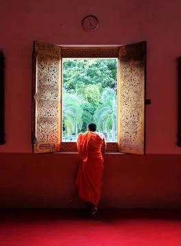 Buddhist monk contemplating through temple window overlooking garden Stock Photos