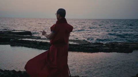 Buddhist monk in red robes on the beach looking into distance Stock Footage 274947017