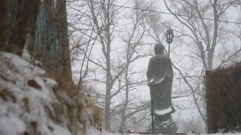 Buddhist Monk Statue in Heavy Snowfall, Back View, Low Angle, Wide shot Stock Footage 231214408