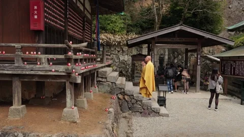 Buddhist monk in yellow robe walking at Katsuoji Temple Osaka with daruma dolls Stock Footage 337777406