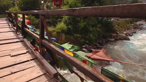 Buddhist prayer flags, fast flowing river and traditional bridge. Pan around Stock Footage 66525574