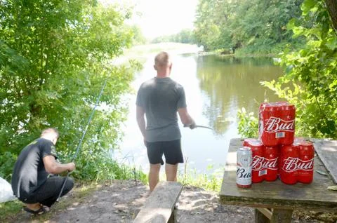 Budweiser Bud beer cans pack on old table and fisherman at river on backgroun Stock Photos