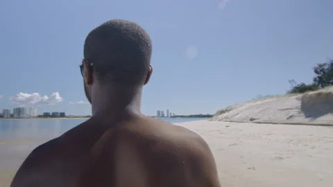Buff black milliennial man walks on sandy beach under blue sky in Australia. Med Stock Footage 199459581