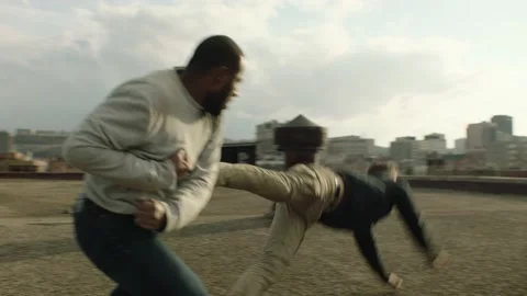 Buff fighter man punches and knocks out another man on a warehouse rooftop in ov Stock Footage 199461373