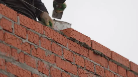 Builder adjusts brick position clearing cement with trowel Stock Footage 311892985