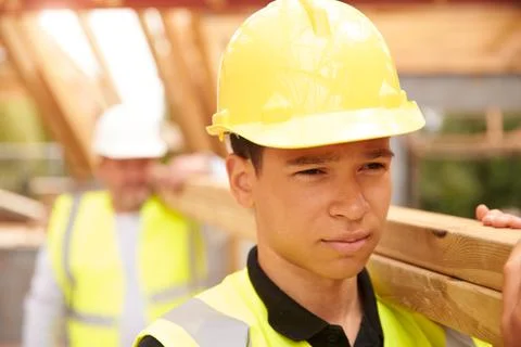 Builder And Apprentice Carrying Wood On Construction Site Stock Photos