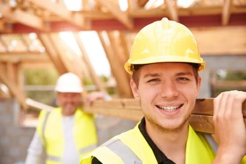 Builder And Apprentice Carrying Wood On Construction Site Stock Photos