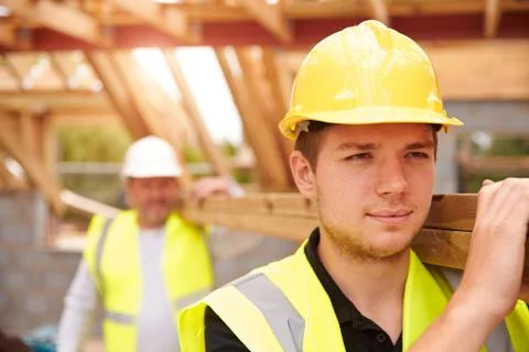 Builder And Apprentice Carrying Wood On Construction Site Stock Photos