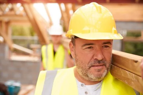 Builder And Apprentice Carrying Wood On Construction Site Stock Photos