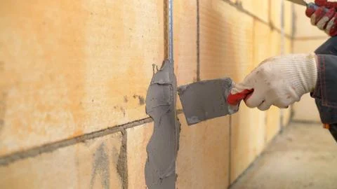 Builder applying plaster on yellow block wall using trowel. Construction wo.. Stock Photos