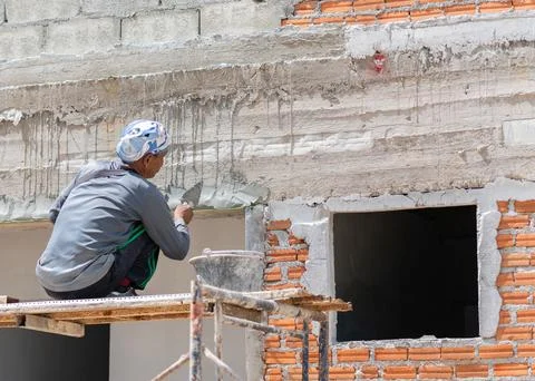 Builder applying wet cement mortar to finish wall surface near window frame.. Stock Photos
