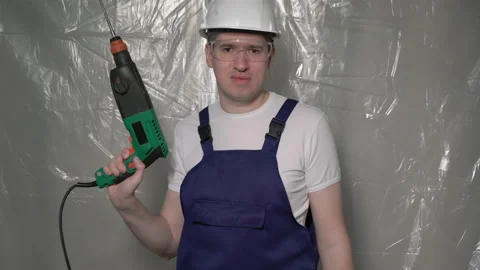 Builder in blue overalls and white hard hat helmet and glasses with perforator. 스톡 동영상 170335657