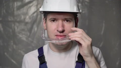 Builder in blue overalls and white hard hat puts on protective glasses. Vidéo 170541314