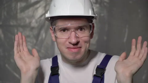 Builder in blue overalls and white hard hat closing face with hands, hiding. Vídeos de archivo 170541353