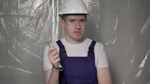 Builder in blue overalls and white hard hat helmet and glasses with wrench. Vidéo 170543093