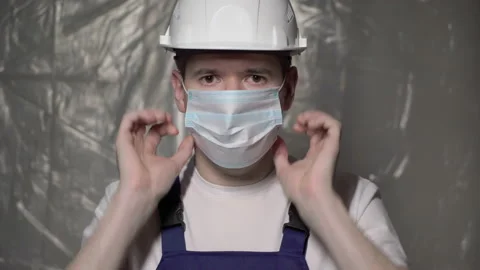 Builder in blue overalls and white hard hat puts on face mask. Vidéo 170567197