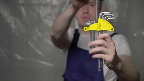 Builder in blue overalls and white hard hat helmet and glasses with hex wrenches Vidéo 170567407