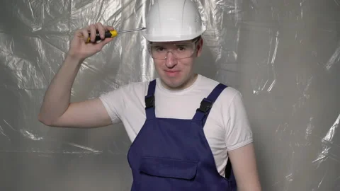 Builder in blue overalls and white hard hat helmet and glasses with screwdriver. Vidéo 170571298