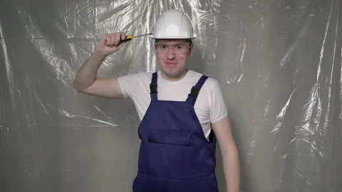 Builder in blue overalls and white hard hat helmet and glasses with screwdriver. 動画素材 170572199