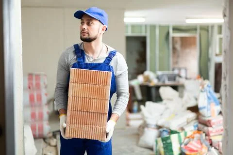 Builder in blue workwear planning erection of partition wall in building under Stock Photos