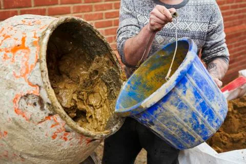 A builder, bricklayer standing next to a cement mixer, holding a blue bucket. Stock Photos