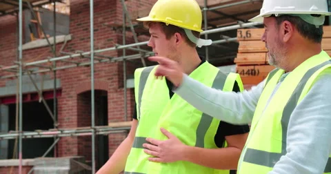 Builder On Building Site Discussing Work With Apprentice Vídeos de archivo 56221279