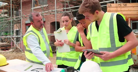 Builder On Building Site Discussing Work With Apprentices Vídeos de archivo 56221350
