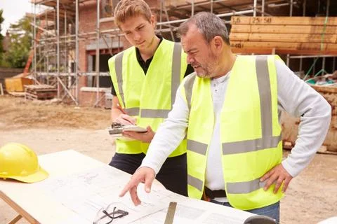 Builder On Building Site Discussing Work With Apprentice 스톡 사진