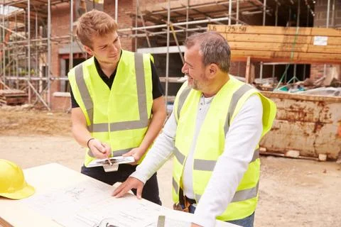 Builder On Building Site Discussing Work With Apprentice Stock Photos