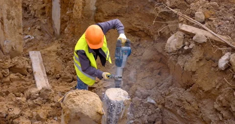 A builder cleaves a piece of a concrete pile with powerful industrial rock drill Stock Footage 147637503