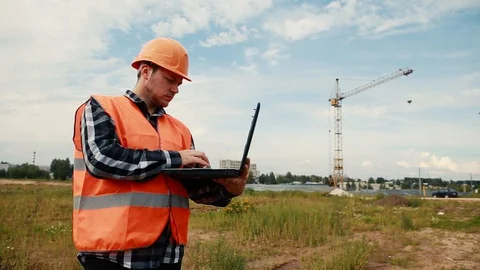 The builder at a construction site in the background of a crane enters data into Stock Footage 129060004