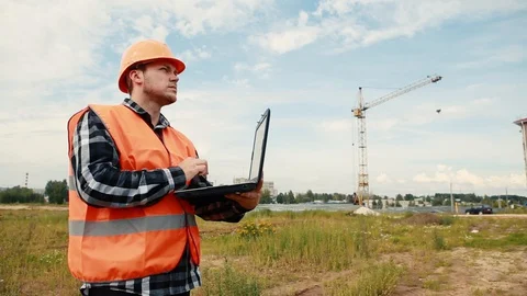 A builder at a construction site in the background of a crane looks at an object Stock Footage 129194169
