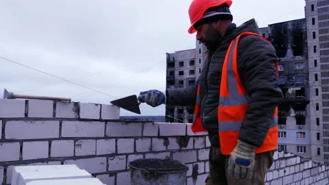 A builder at a construction site lays cement and lays bricks on it, builds a Stock Footage 228055079