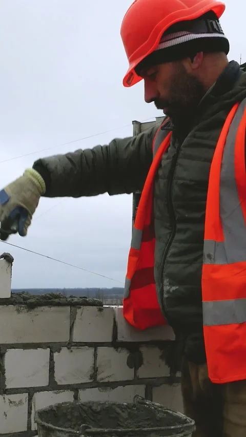 A builder at a construction site lays cement and lays bricks on it, builds a Video stock 311975953