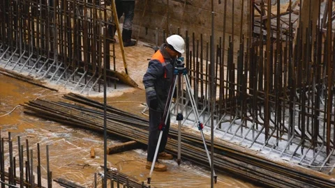 A builder at a construction site looks at a measuring device and sets the level Stock Footage 262477799