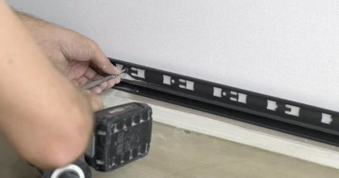 Builder deftly twists screws into drilled holes in wall, fastens skirting, work Stock Footage 131181584