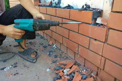 The builder dismantles the brick in the wall with a punch 스톡 사진