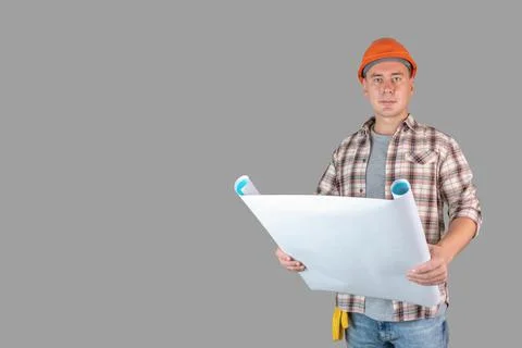 A builder with a drawing in his hands stands on a gray background and looks i Stock Photos