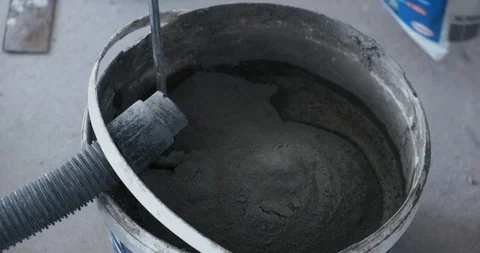 Builder with electric appliance stirs mortar for laying tiles, plastic bucket Stock Footage 129840239