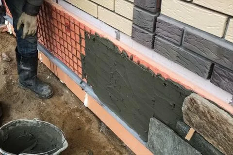 Builder faces the basement of a house with a wild stone. Flat fo Stock Photos