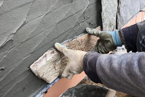 Builder faces the basement of a house with a wild stone. Flat fo Stock Photos