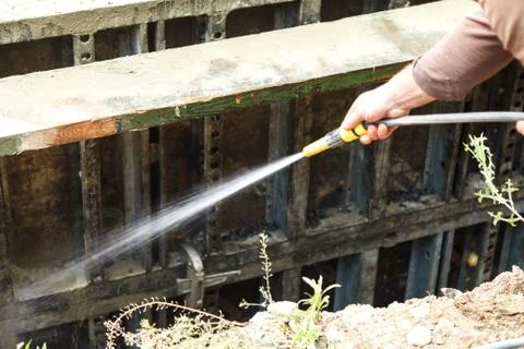 The builder flushes the metal formwork shield with water from the hose 스톡 사진