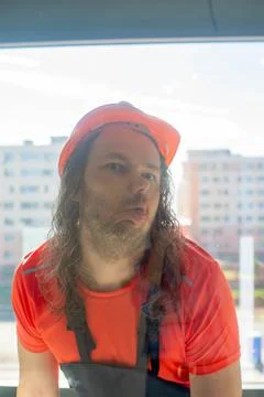 A builder in gloves in a helmet makes a face behind the glass Stock Photos